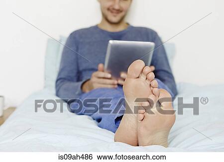 Mid adult man lying on bed using digital tablet View Large Photo Image Stock Photograph - Mid adult man lying on bed using digital tablet. Fotosearch