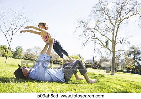 Stock Image - Mid adult man playing with daughter in park. Fotosearch