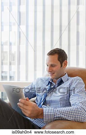 Picture - Mid adult man relaxing at home with digital tablet. Fotosearch