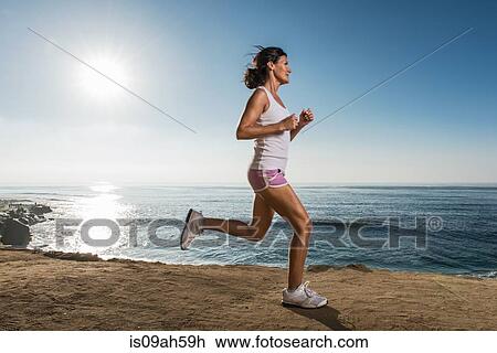 Stock Image - Mid adult woman jogging along cliff. Fotosearch