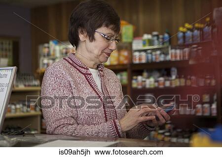Stock Image - Owner of health foods store using smartphone. Fotosearch