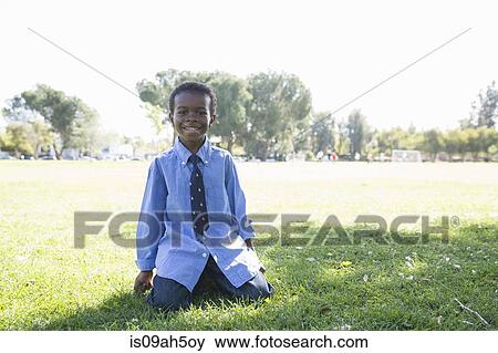 Stock Photo - Portrait of boy kneeling on grass in sunlit park. Fotosearch