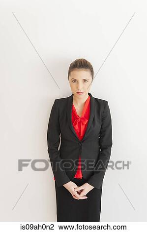 Stock Image - Portrait of young businesswoman in front of white office wall. Fotosearch