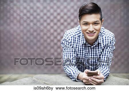 Stock Photo - Portrait of young man holding smartphone. Fotosearch