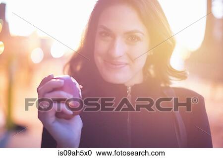 Stock Image - Portrait of young woman eating an apple on the street. Fotosearch