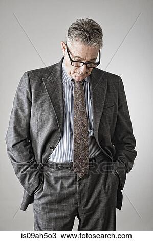 Stock Image - Senior man with hands in pockets, looking down. Fotosearch