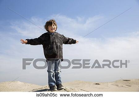 Smiling boy standing on sand with arms outstretched View Large Photo Image Stock Image - Smiling boy standing on sand with arms outstretched. Fotosearch