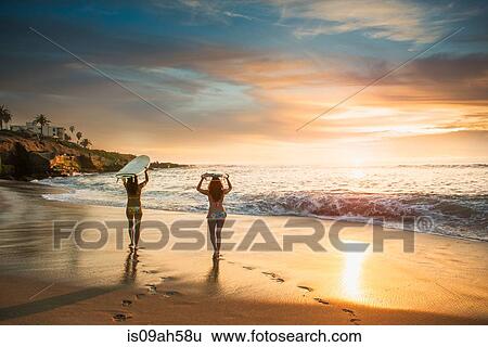 Surfers carrying surf board, walking along beach View Large Photo Image Stock Photograph - Surfers carrying surf board, walking along beach. Fotosearch