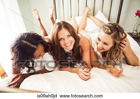 Stock Image - Three female friends lying on bed. Fotosearch