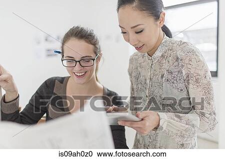 Stock Image - Two female colleagues discussing blueprint. Fotosearch