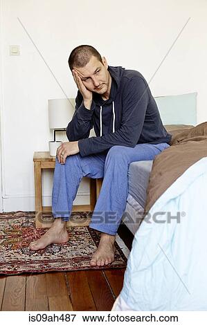 Stock Photo - Unhappy mid adult man sitting on bed with head in hand. Fotosearch