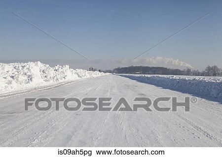 Stock Image - View of empty snow covered highway in sunlight. Fotosearch