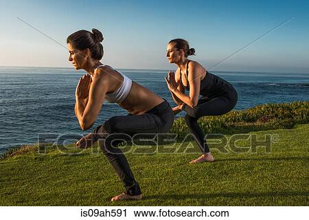 Stock Image - Women on cliff, in yoga positions. Fotosearch
