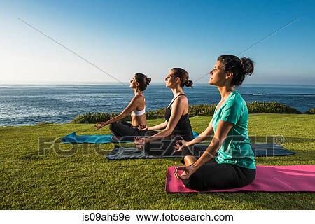 Stock Image - Women on cliff, meditating. Fotosearch