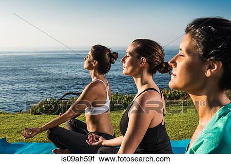 Stock Image - Women on cliff, meditating. Fotosearch