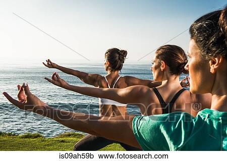 Stock Image - Women on cliff, practising yoga. Fotosearch