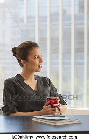 Stock Photo - Young businesswoman having a coffee break in office. Fotosearch