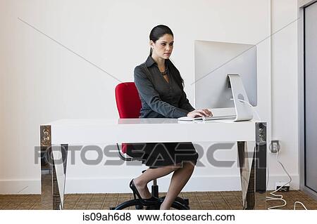 Young businesswoman sitting at desk, using computer View Large Photo Image Stock Photo - Young businesswoman sitting at desk, using computer. Fotosearch