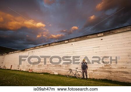 Picture - Young man standing next to white wall with his bicycle. Fotosearch