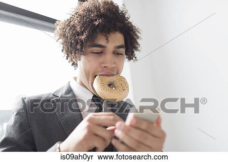 Young man using cell phone with bagel in mouth View Large Photo Image Stock Photography - Young man using cell phone with bagel in mouth. Fotosearch