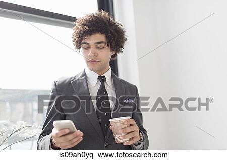 Stock Photography - Young man using cell phone with coffee. Fotosearch
