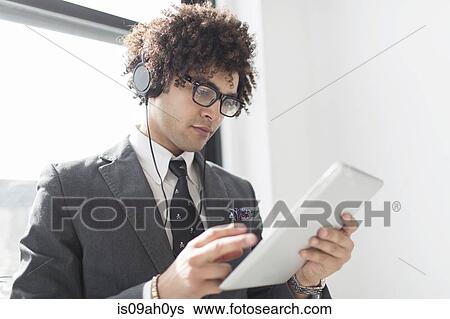 Young man wearing headphones using digital tablet View Large Photo Image Stock Photograph - Young man wearing headphones using digital tablet. Fotosearch