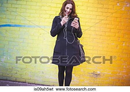 Stock Photograph - Young woman choosing music on city street. Fotosearch