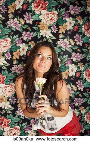 Young woman holding rose in front of floral wallpaper View Large Photo Image Stock Image - Young woman holding rose in front of floral wallpaper. Fotosearch