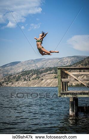 Stock Image - Young woman jumping into Okanagan Lake, Naramata, British Columbia, Canada. Fotosearch