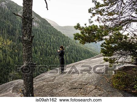 Stock Image - Young woman looking at smartphone, Squamish, British Columbia, Canada. Fotosearch