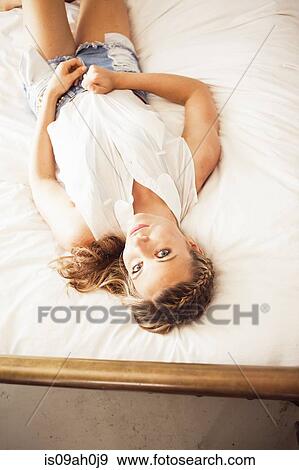 Stock Photo - Young woman lying on bed looking at camera. Fotosearch