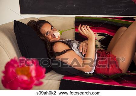 Young woman lying on sofa holding rose View Large Photo Image Stock Image - Young woman lying on sofa holding rose. Fotosearch