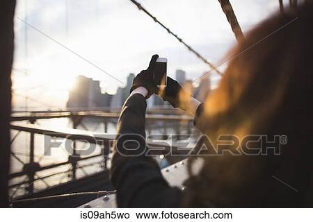 Picture - Young woman photographing city on smartphone, New York, USA. Fotosearch