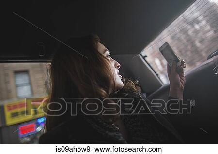 Stock Photo - Young woman taking photograph on cellphone from taxi. Fotosearch