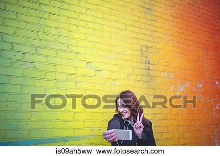 Stock Photo - Young woman taking self portrait next to yellow wall. Fotosearch