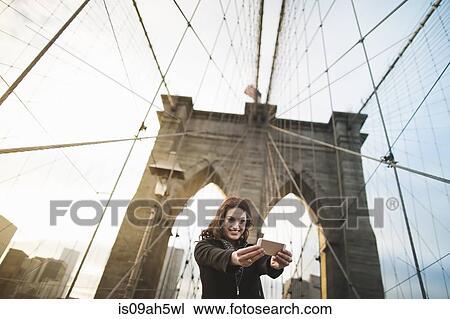 Young woman taking self portrait on Brooklyn bridge, New York, USA View Large Photo Image Stock Image - Young woman taking self portrait on Brooklyn bridge, New York, USA. Fotosearch
