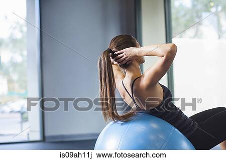 Stock Image - Young woman working out with gym ball. Fotosearch