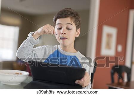 Boy looking at digital tablet whilst eating breakfast View Large Photo Image Stock Photograph - Boy looking at digital tablet whilst eating breakfast. Fotosearch