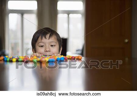 Stock Image - Boy peering over table at candy. Fotosearch