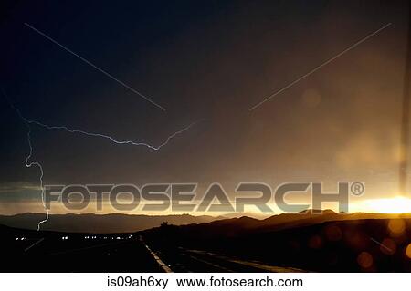 Stock Photo - Car headlights on silhouetted highway during thunderstorm. Fotosearch