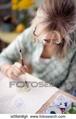 Stock Image - Close up of mature female artist watercolour painting in studio. Fotosearch