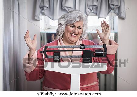 Stock Photography - Happy mature woman on bathroom weighing scales. Fotosearch