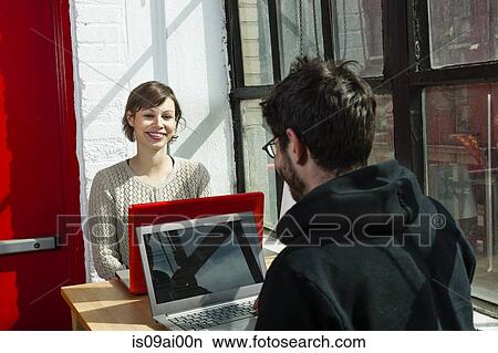 Picture - Male and female designers chatting over laptops in studio. Fotosearch