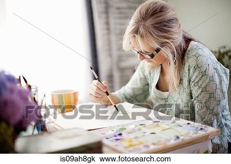 Stock Image - Mature female artist watercolour painting in studio. Fotosearch