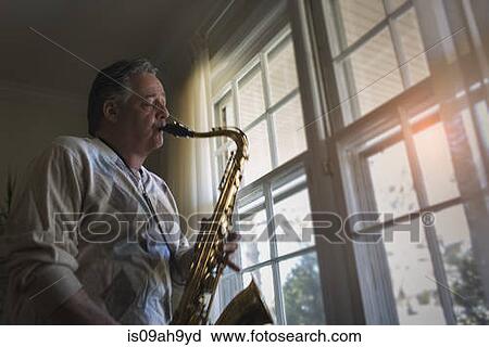 Stock Image - Mature man at home playing saxophone. Fotosearch