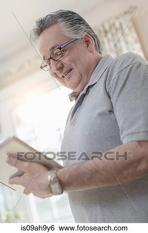 Stock Photograph - Mature man at home using digital tablet. Fotosearch