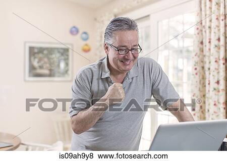 Stock Photo - Mature man celebrating whilst looking at laptop. Fotosearch