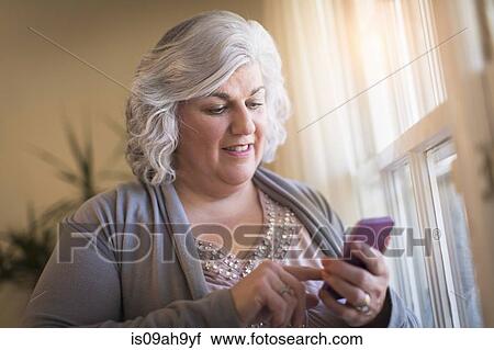 Mature woman at home texting on her cellphone View Large Photo Image Stock Image - Mature woman at home texting on her cellphone. Fotosearch