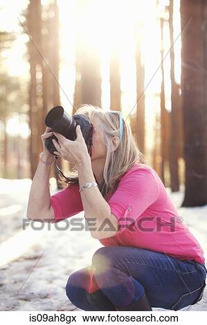 Stock Photo - Mature woman photographing in forest. Fotosearch