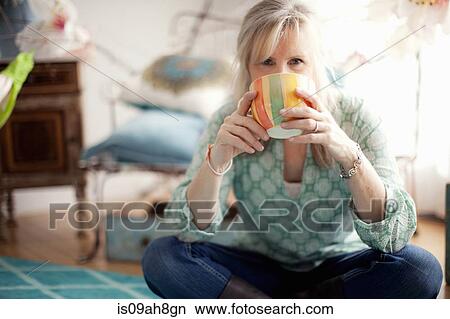 Mature woman sitting cross legged drinking coffee View Large Photo Image Picture - Mature woman sitting cross legged drinking coffee. Fotosearch